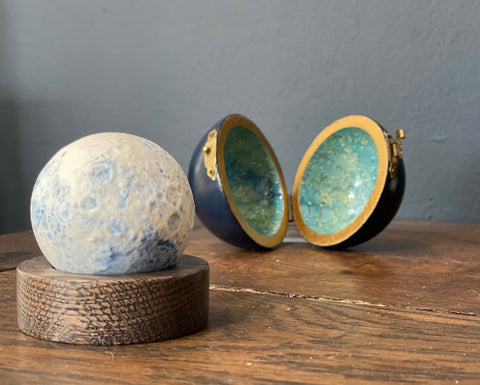 minature ceramic blue moon on a wooden stand with a round case behind it is made by Loraine Rutt of the Little Globe company 