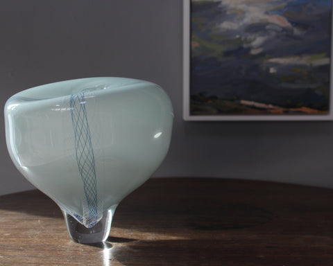 pale blue round glass vessel next to corner of landscape painting 