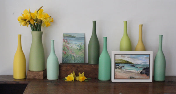 Collection of ceramics by Lucy Burley in shades of yellows and greens with daffodils in a sage coloured vase