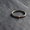 a narrow ring in oxidised silver with small gold dot by Lucy Spink, British jewellery designer.