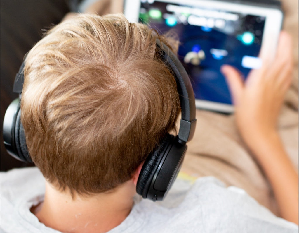 A boy listening to blue headphones watches an iPad, viewed from behind.