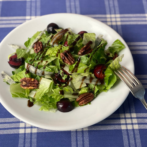 Chopped romaine lettuce is dressed with halved fresh cherries, toasted pecans, sliced blue marble jack cheese, and a vinaigrette