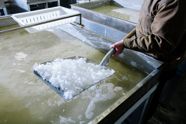 Close up of a shovel-full of flake salt crystals being lifted from a evaporation pan.