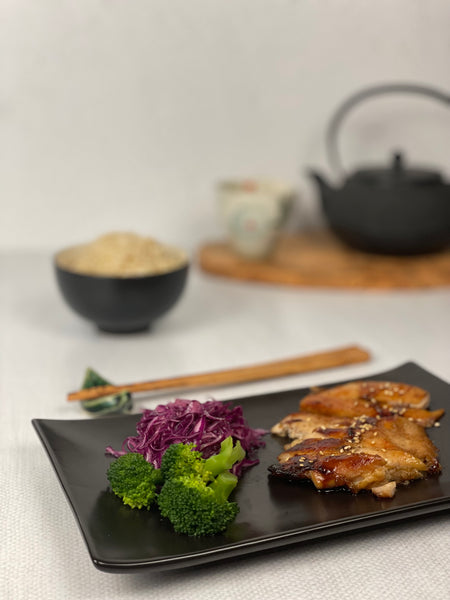 Teriyaki chicken, broccoli and miso cabbage shown in foreground with rice and tea in the back.