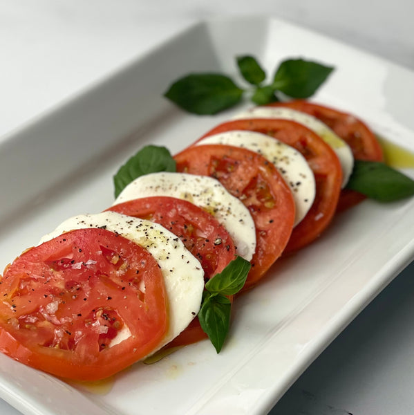 Classic Insalata Caprese with rounds of round red tomato slices tucked between rounds of mozzarella with bits of basil and olive oil finish.