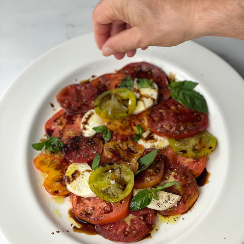 Donald sprinkles flaked salt on top of a classic caprese onto which we've poured balsamic vinegar