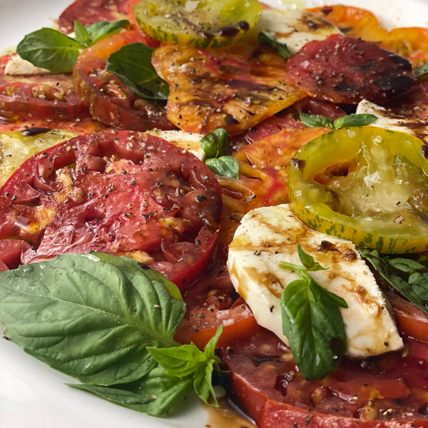 Close up of an heirloom tomato Caprese salad with Mozzarella, basil, and olive oil. Balsamic vinegar has been added.