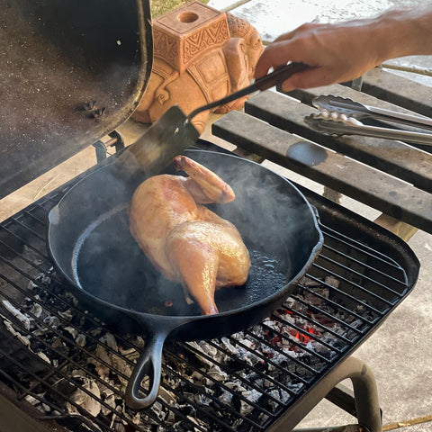 Half chicken in a 12" cast iron pan, on an outdoor grill