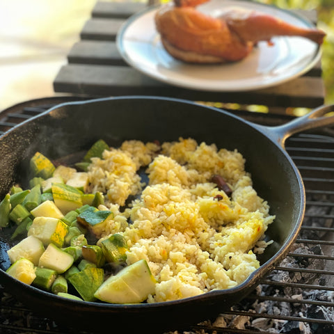 Fresh summer squash, okra, and leftover spiced saffron basmati rice in a 12" cast iron skillet on an outdoor grill