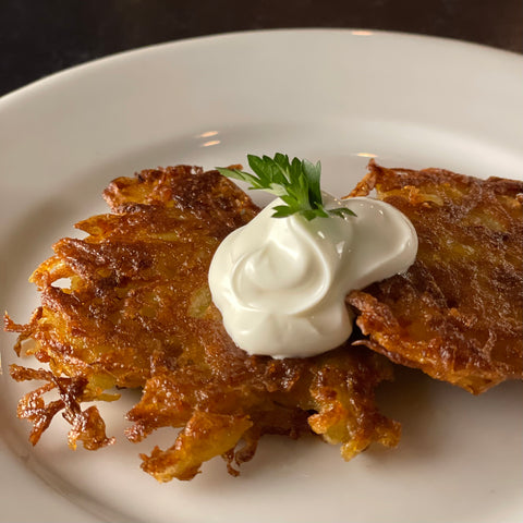 Two potato latkes with sour cream and a sprig of parsley on a simple porcelain plate