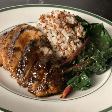 A small dinner plate holds several sauced slices of pork tenderloin, with a highly textured sprinkle of roasted spices on top, a rice and red quinoa blend, and Swiss chard