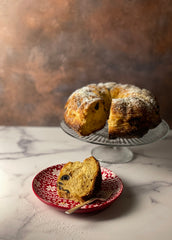 A single slice of brioche is placed on a dessert plate embossed with a Fair Isle design and the entire round bread is behind it on a glass pedestal.