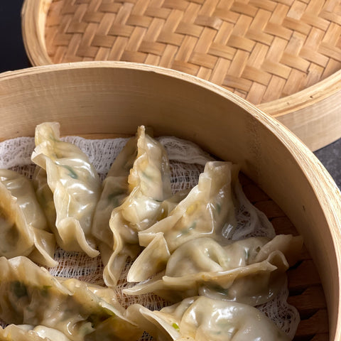 A bamboo steamer is opened to reveal 8 steamed dumplings