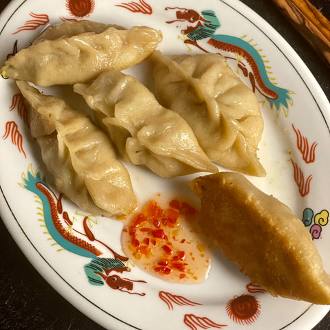 Five dumplings on a dragon plate. One is turned so you can see the fried underside, and it is next to a pool of Firecracker sauce.