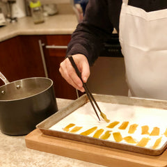 Donald uses chopsticks to move pomelo peel, cooking in sugar syrup, into a sheet pan of granulated sugar