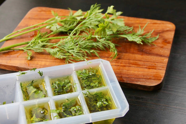 plastic ice cube tray is partially filled with chopped herbs and olive oil, and just beyond is a small wooden cutting board with a few bunches of assorted fruit herbs.