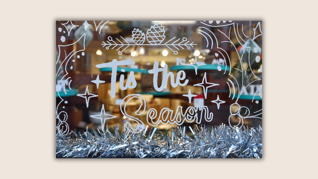 A pale background with one central rectangular picture. The picture shows a Christmas window display with white cursive font reading 'Tis the Season', with silver tinsel. The picture has a shadow effect.