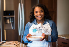 Erin Issac stands wearing an apron and holding a mixing bowl smiling at the camera.