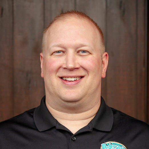 Matt Riopelle, Pederson's Farms National Sales Manager, stands smiling against a dark wood background.