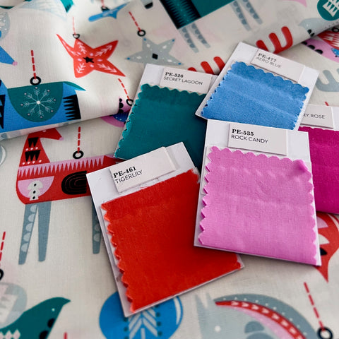 orang, pink, blue and green fabric swatches on some Christmas patterned fabric.