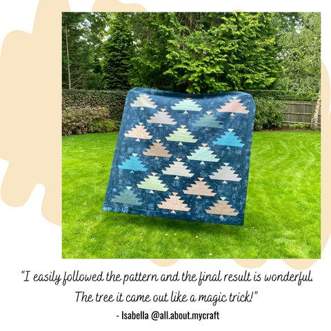a large quilt top in navy blue featuring multi coloured trees displayed in a garden