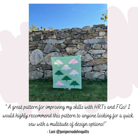 A pastel green baby sized quilt top featuring pink and green christmas trees displayed against a stone wall
