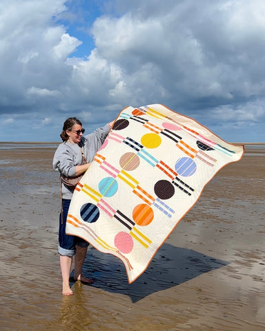 A woman holding a quilt with circle on a windy beach