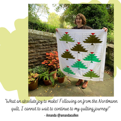 A young woman holding a baby sized quilt top featuring green christmas trees
