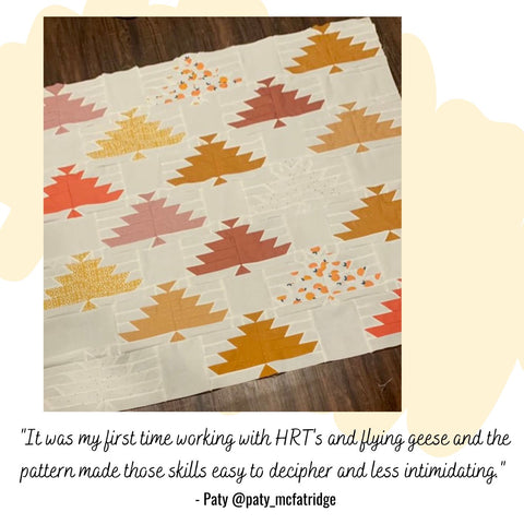 a scrappy quilt featuring trees in autumnal colours laid out on a floor