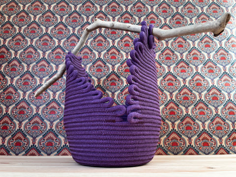 basket made of purple rope with a piece of driftwood for the handle.