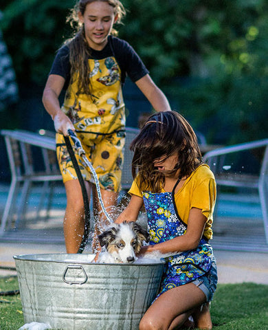 Two young girl washing their dog while wearing Splash Fabric aprons