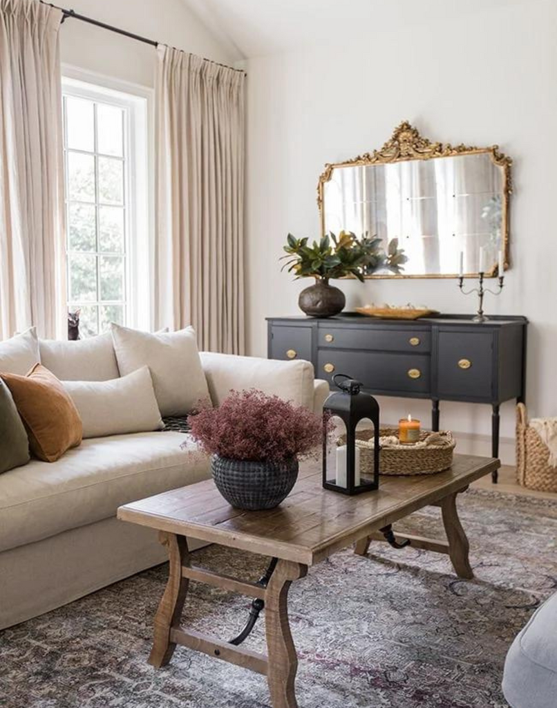 Mix high and low decor styles to create a collected home style. Living room scene with designer credenza, ornate gold mirror, wooden coffee table styled with decor pieces and light colored couch.
