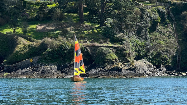 A Fowey River wooden sailing boat with an orange black & yellow sail