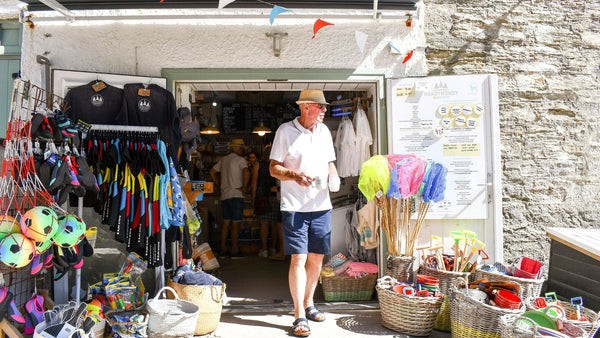 A man wearing shorts walking out of Readymoney Beach Shop on a sunny day