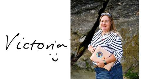 Victoria owner of Readymoney Beach Shop standing against some rocks holding her laptop and smiling