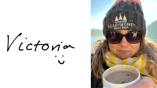 a selfie of victoria at Readymoney Cove wearing a bobble hat and sunglasses and holding a hot chocolate