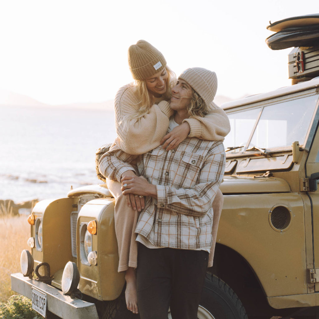 Woman and man with long hair wearing beanies sitting on a jeep while on a roadtrip