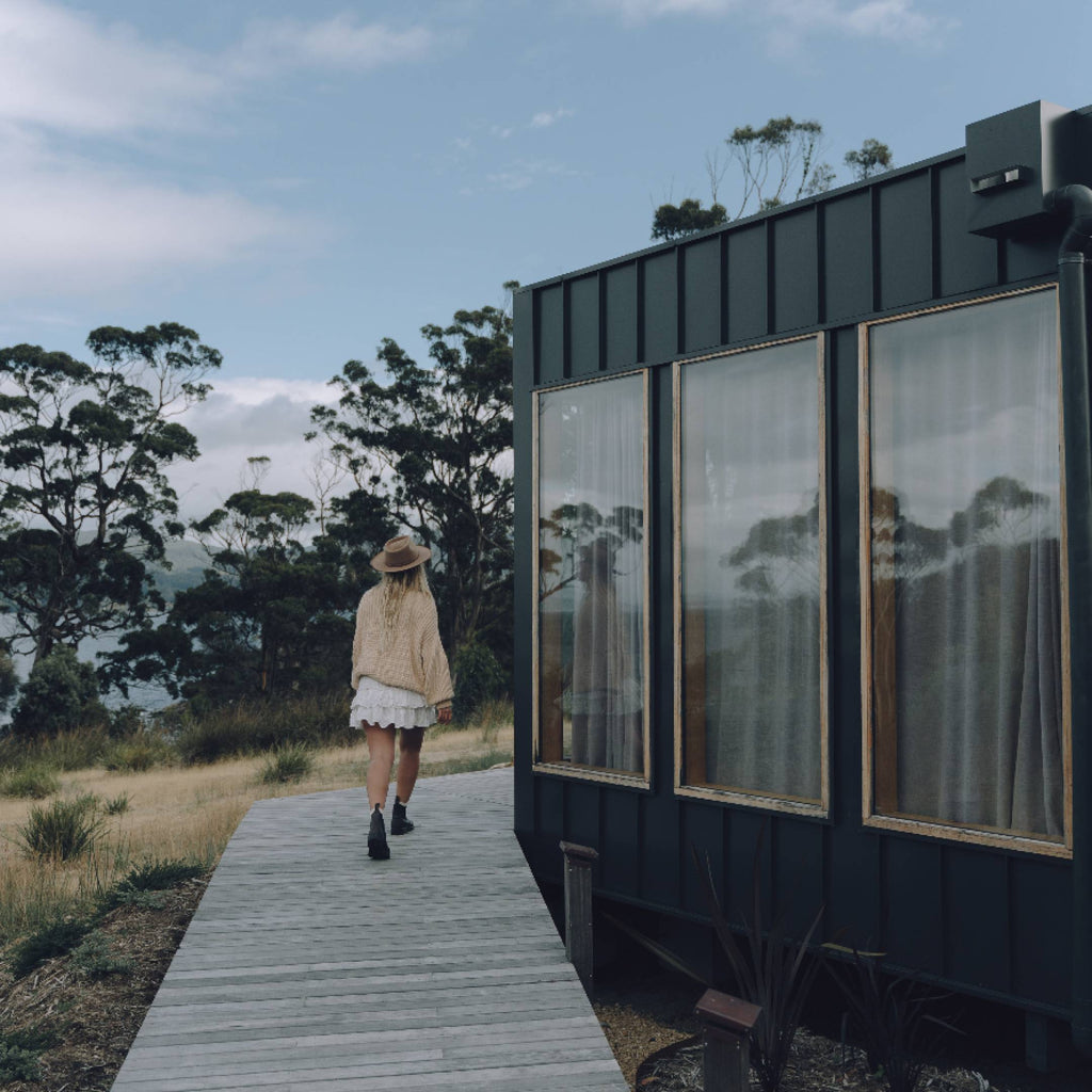 Women with long blonde hair wearing a wide brim wool hat walking next to a cabin