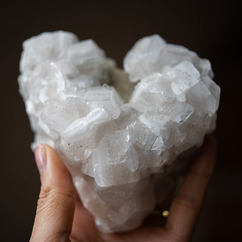 A close up image of a naturally heart-shaped flourite and pyrite heart bring held by against a black background.