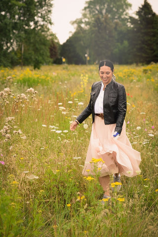 Woman walking through a field of flowers in black leather jacket and pink tulle skirt.