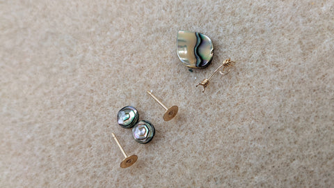 Overhead view of abalone components for jewelry and gold components on a work table.  One pair of faceted 