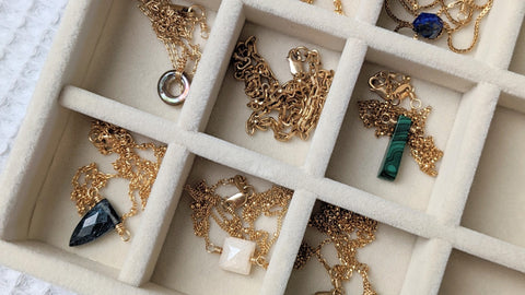 Overhead close up view of 14K gold fill gold gemstone necklaces in light beige velvet jewelry drawer. 