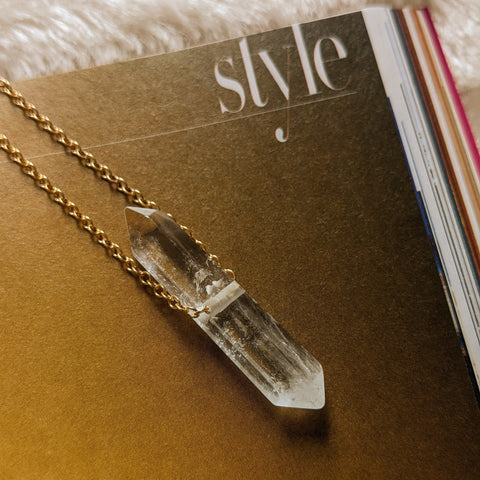 Zurina Ketola's Threaded Crystal Energy Necklace. Close up of quartz pendant on warm yellow background. t 
