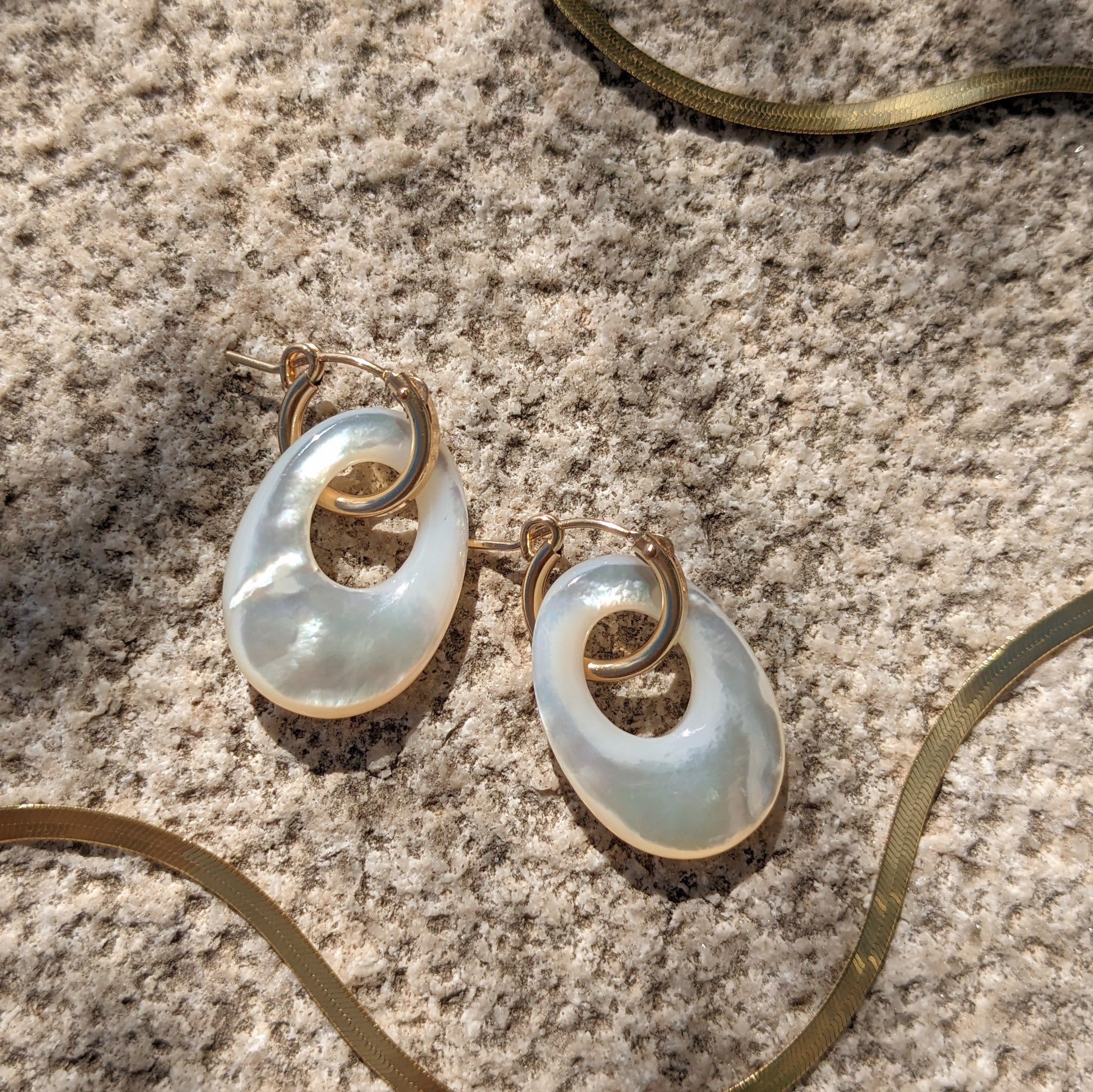 Close up image of the Ellipical Huggie Hoops from jewelry designer Zurina Ketola in 14K gold fill and mother of pearl details.