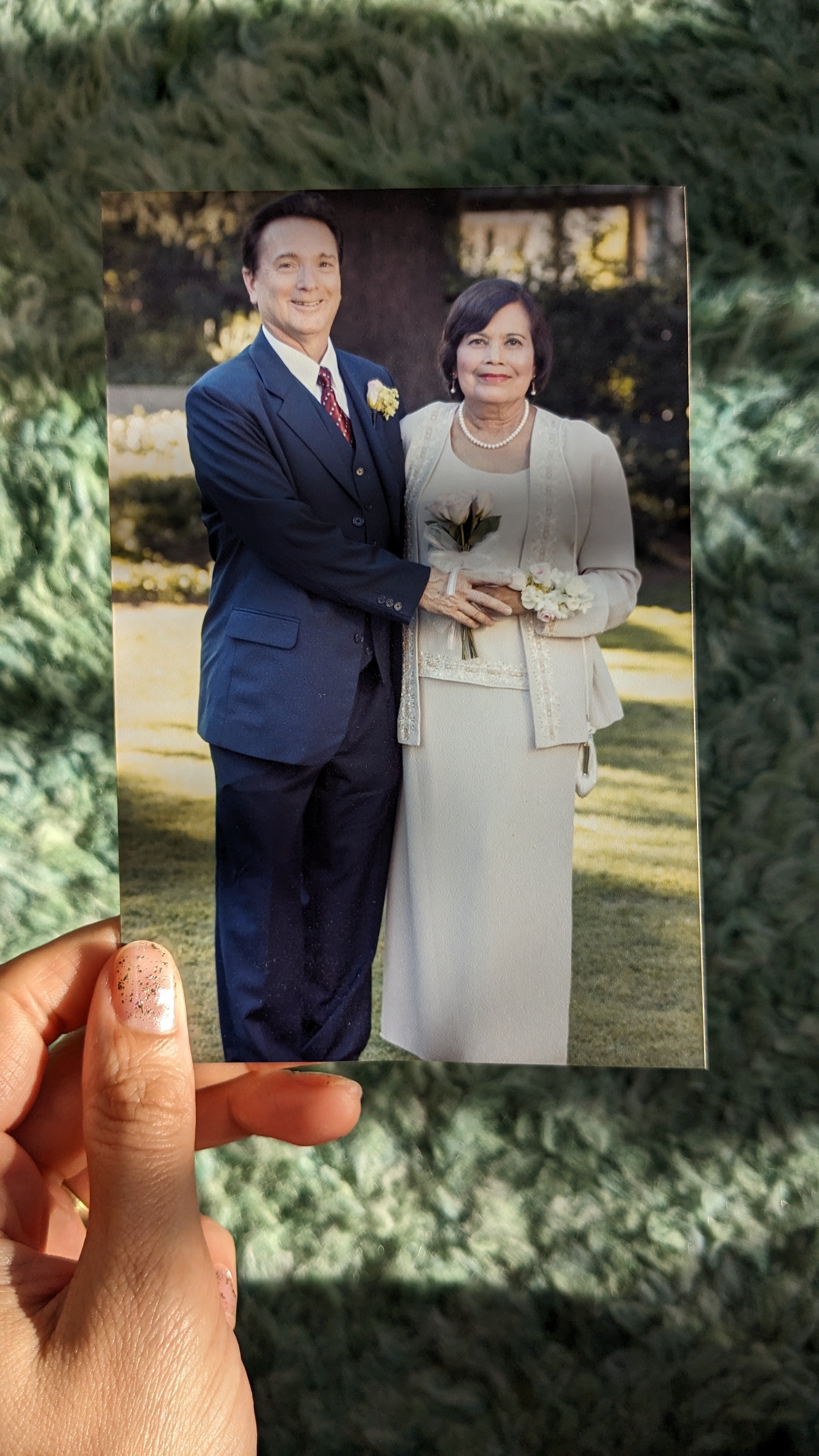 A photograph being held in sunlight over a colorful background of an older couple at their daughter's wedding.