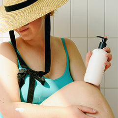woman applying sunscreen and wearing a sun hat for skin protection