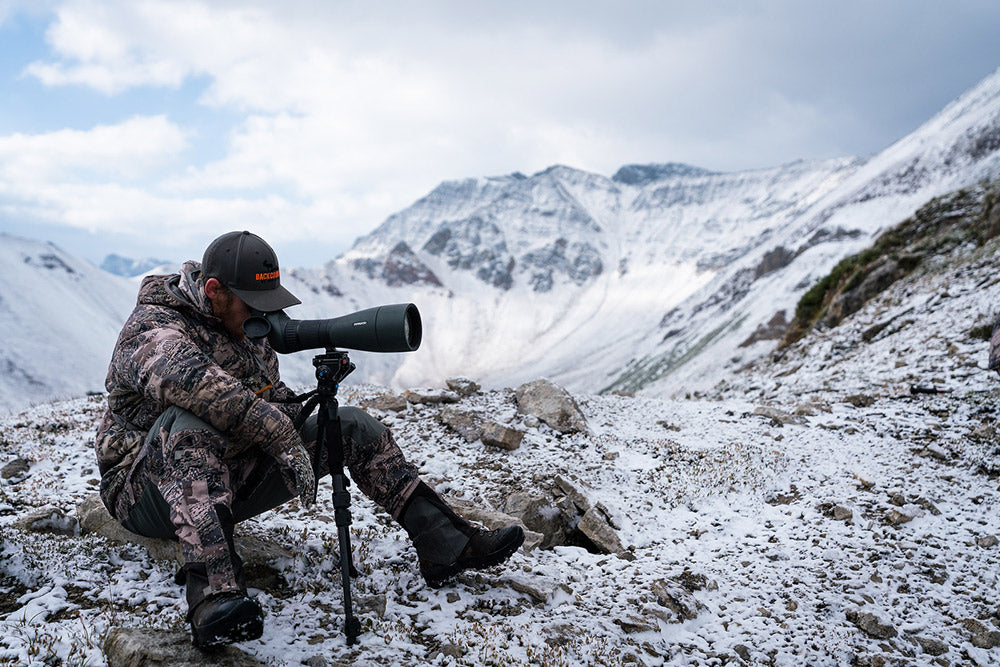 Sitka Gear - Man sitting on mountain top wearing Sitka Blizzard GTX gloves looking through a scope