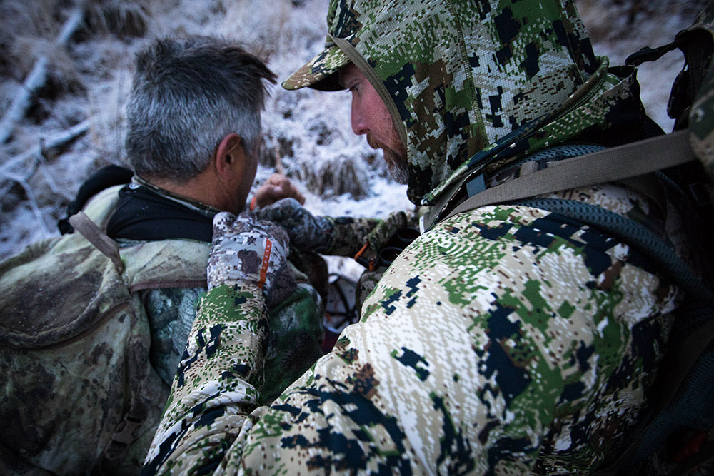 Sitka Gear - man wearing Mountain Jacket adjusting a strap on another man - snow in the background