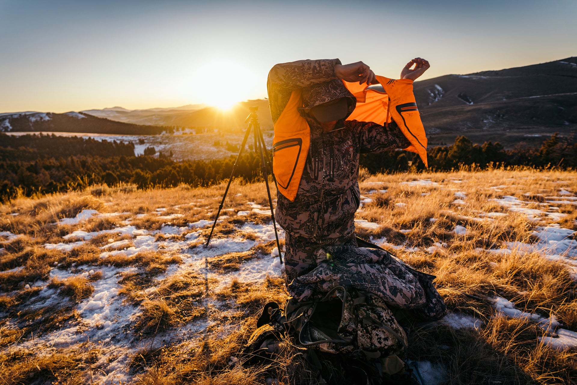 Sitka gear - man knelling putting on a ballistic vest over the Jetstream jacket while the sun rises