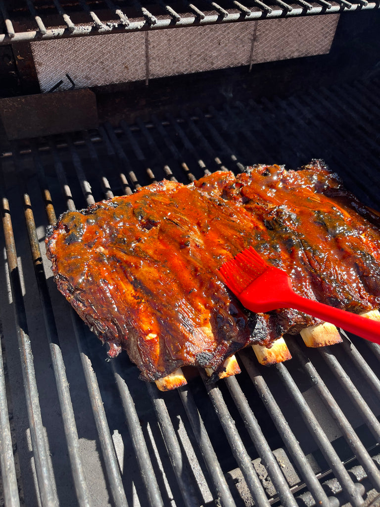 Bison ribs on the grill being basted with barbecue sauce